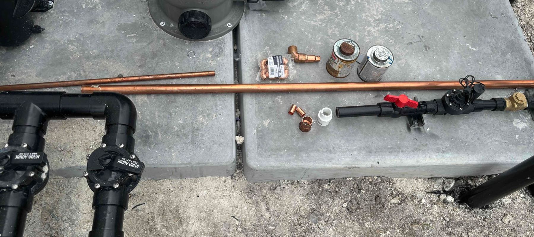 Plumbing tools and copper pipes laid out on a concrete surface for installation