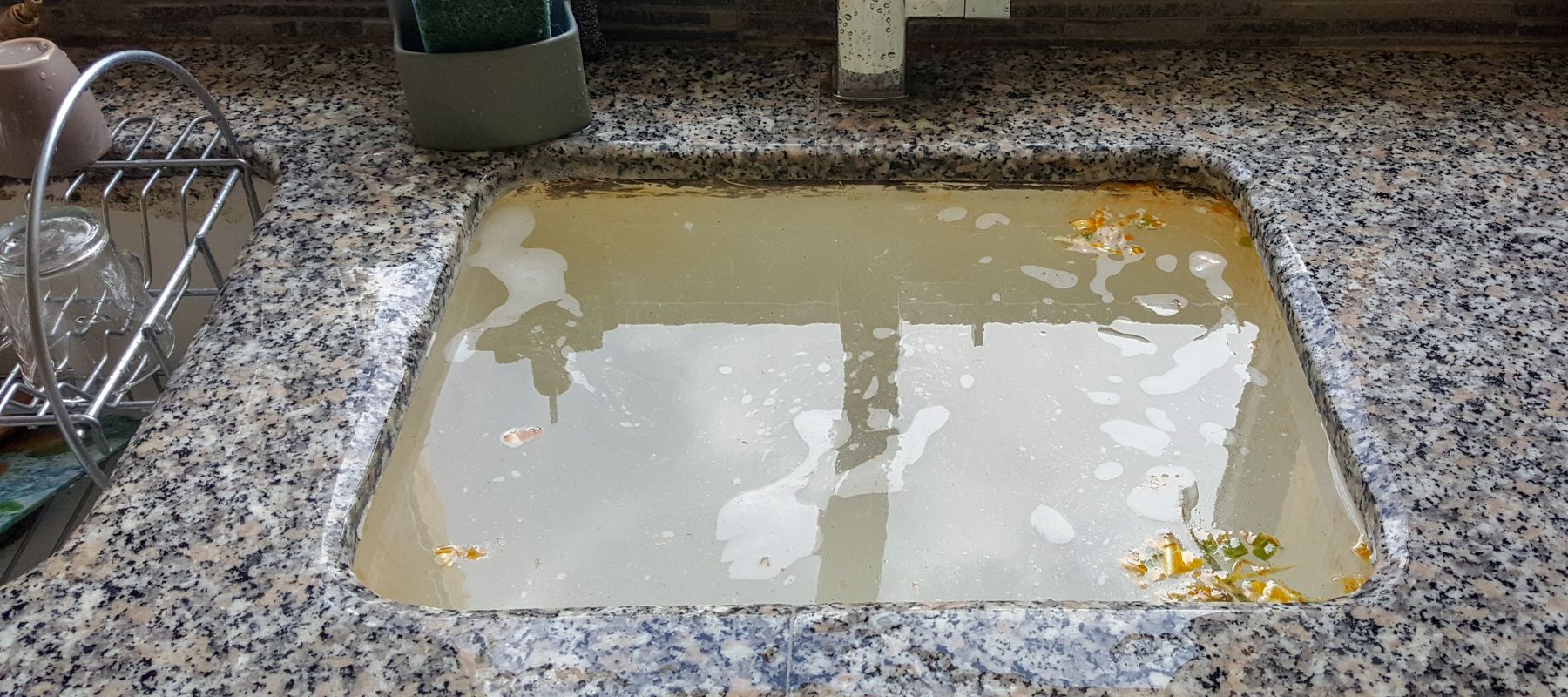 A kitchen sink filled with dirty, stagnant water and food debris, indicating a clogged drain issue