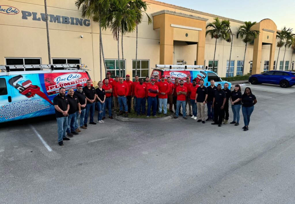 Joe Cole Plumbing team standing in front of company service vehicles outside headquarters