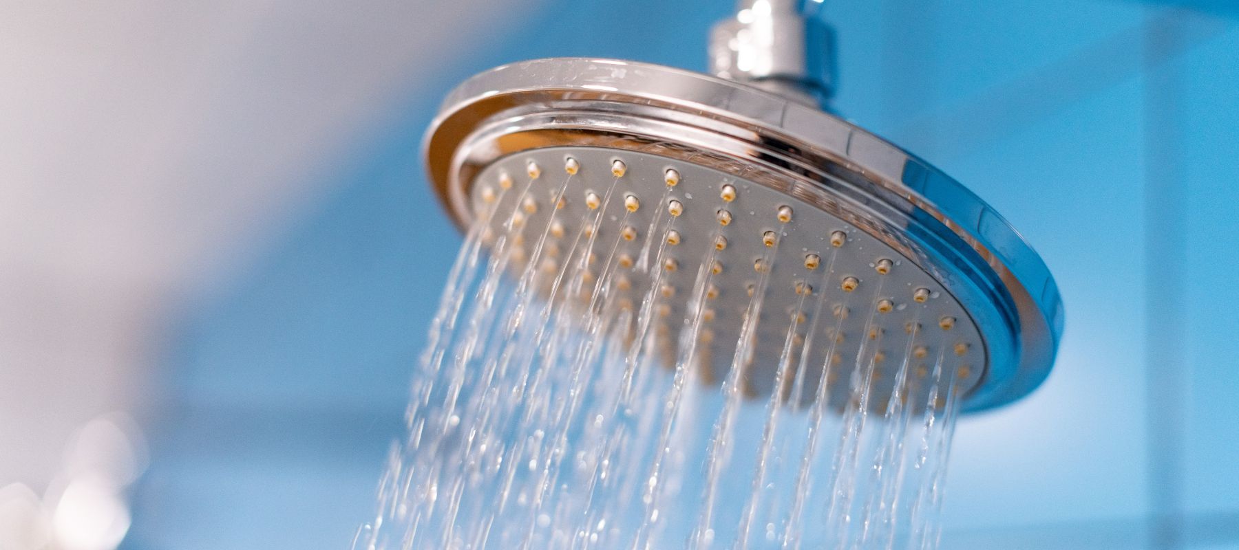 closeup of a round shower head with water running out of it in front of a blue background